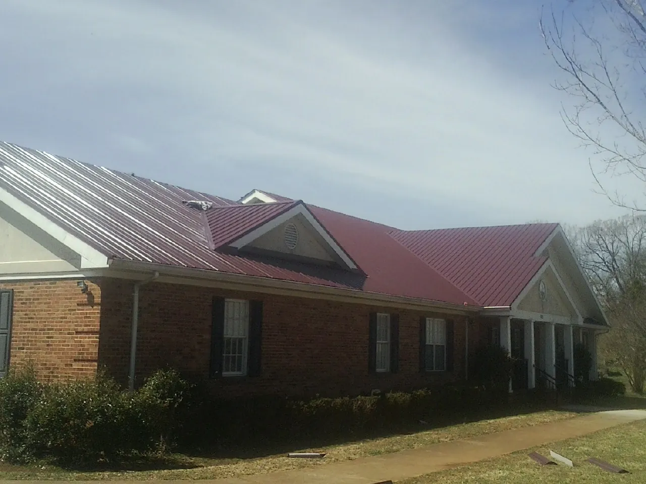Red metal roof with gabled entries on a long brick building, from a Hail Damage Roof Repair job in Narrowsburg
