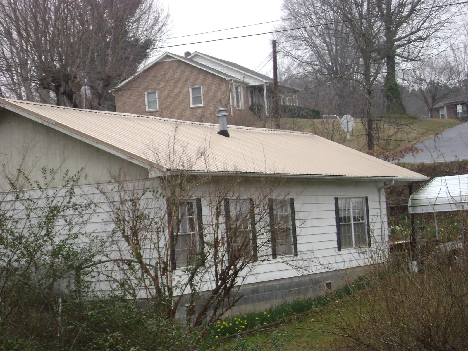 Tan metal roof on a white sided house set into a hillside — Commercial Roofing by Roofing Brothers in Narrowsburg
